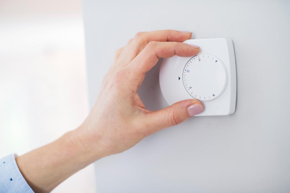 Woman's hand adjusting a central heating thermostat.