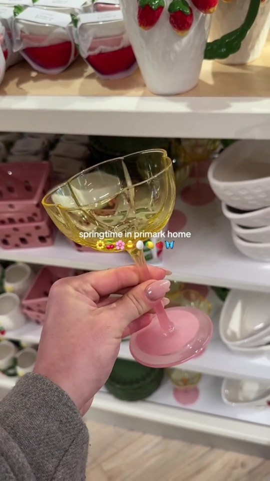 A hand holding a yellow glass with a pink base, surrounded by Primark's spring homeware.