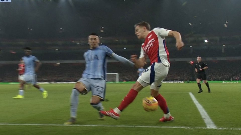 Soccer player in red jersey dribbling the ball, challenged by a player in a light blue jersey.