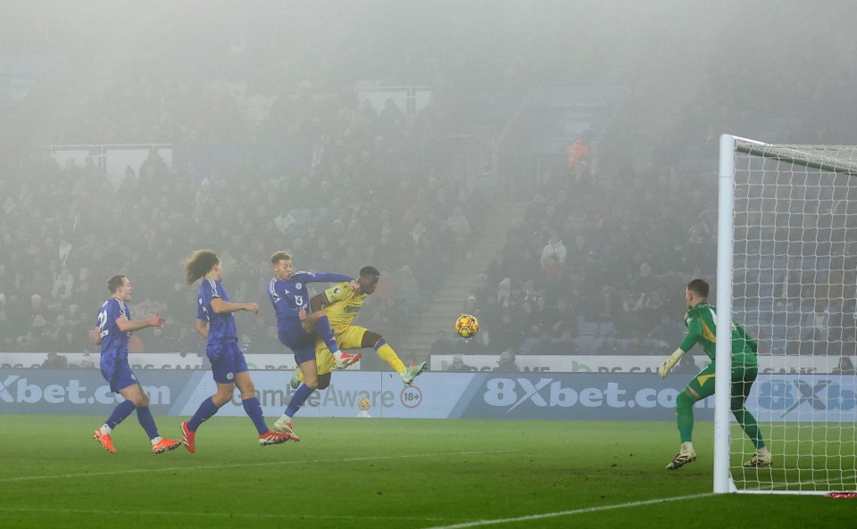 A soccer player scoring a goal in a foggy stadium.