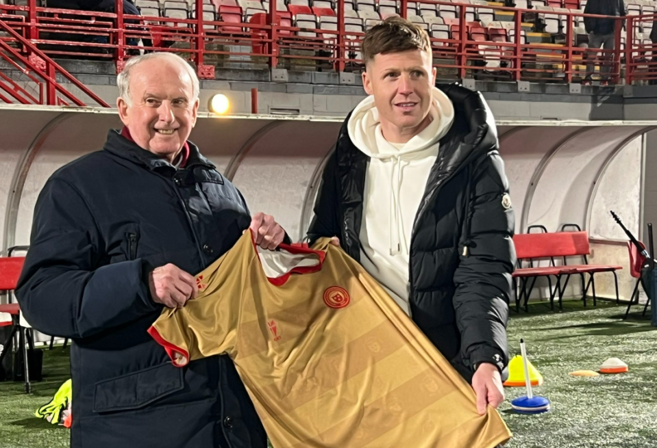 Two men holding a gold soccer jersey.